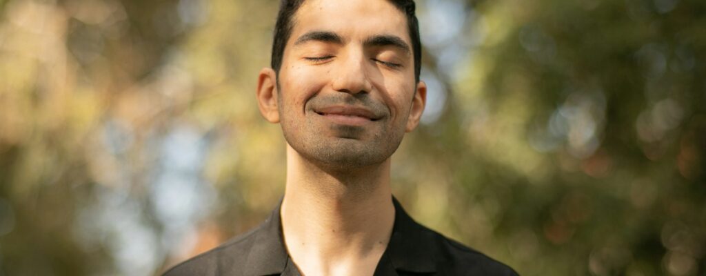 a man with his eyes closed standing in front of trees